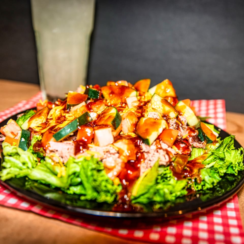 A vibrant salad with lettuce, pulled pork, diced vegetables, and barbecue sauce on a black plate.