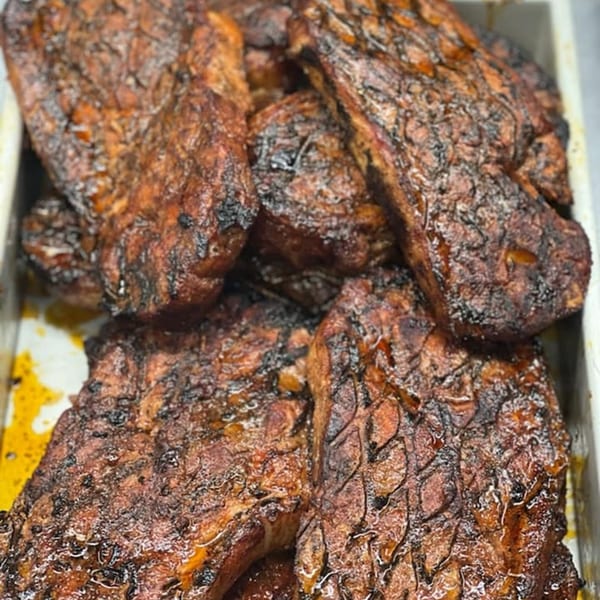 Close-up of several pieces of dark, charred BBQ meat in a metal tray.