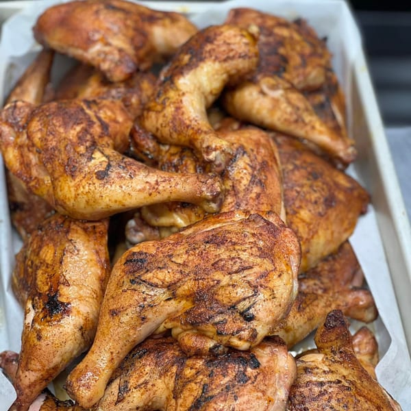Close-up of a white tray filled with numerous golden-brown, grilled B2Q BBQ chicken pieces.