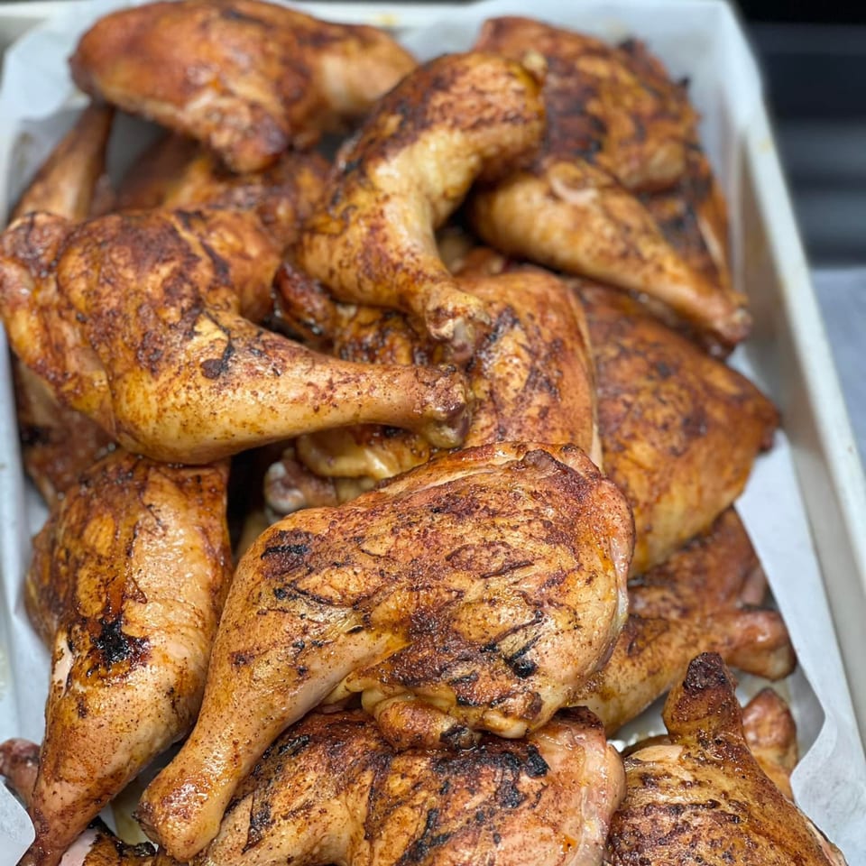Close-up of a white tray filled with numerous golden-brown, grilled B2Q BBQ chicken pieces.