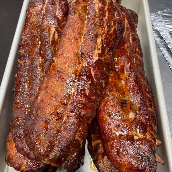 Three racks of glistening, dark brown BBQ ribs in a white pan, ready to be served.