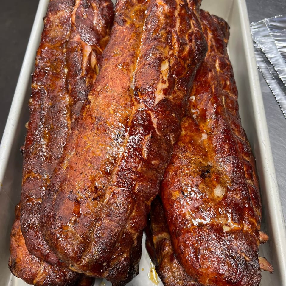 Three racks of glistening, dark brown BBQ ribs in a white pan, ready to be served.