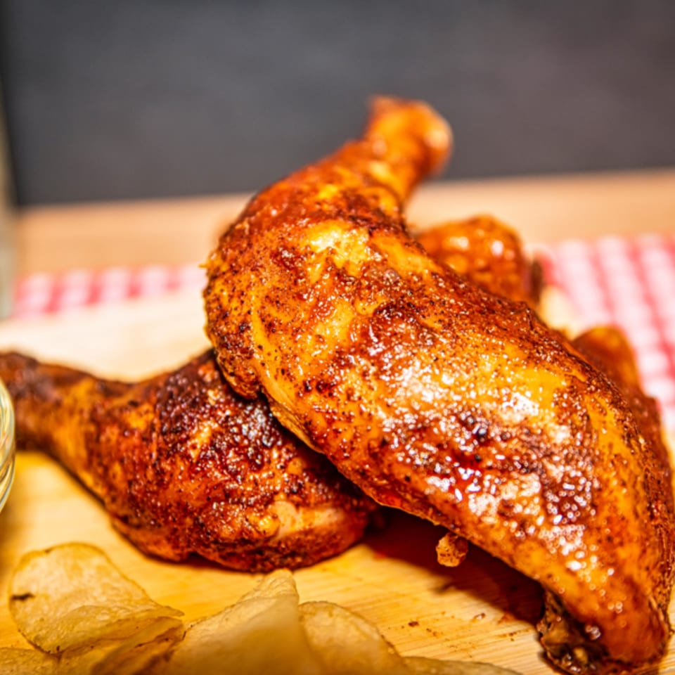 Two crispy, seasoned chicken drumsticks and thighs on a wooden board with potato chips.